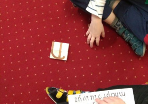 Litera u ułożona z klocków. Chłopiec pokazuje literę u na kartce z instrukcją do układania liter
